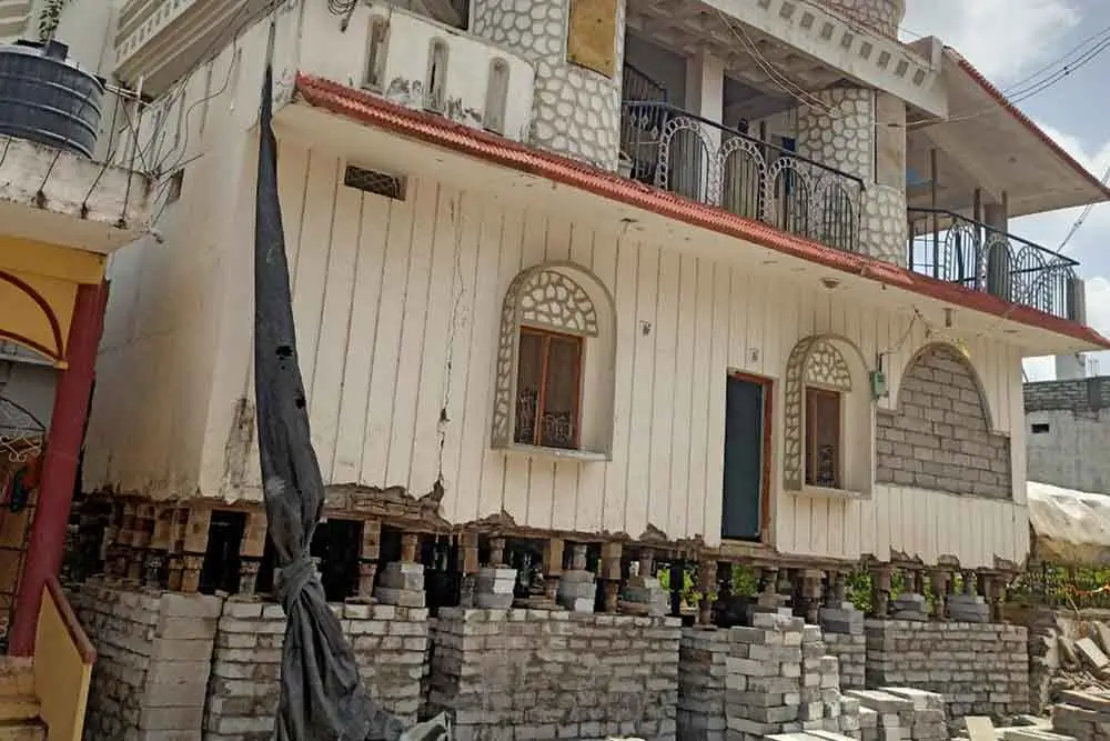 SRBL house lifting service using hydraulic jacks to elevate a residential structure with balcony and windows – ensuring structural integrity and safety.