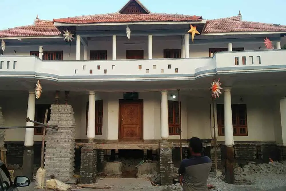 SRBL house lifting service in progress with hydraulic jacks – person standing near elevated porch and structural columns during residential foundation elevation in Uttrakhand.